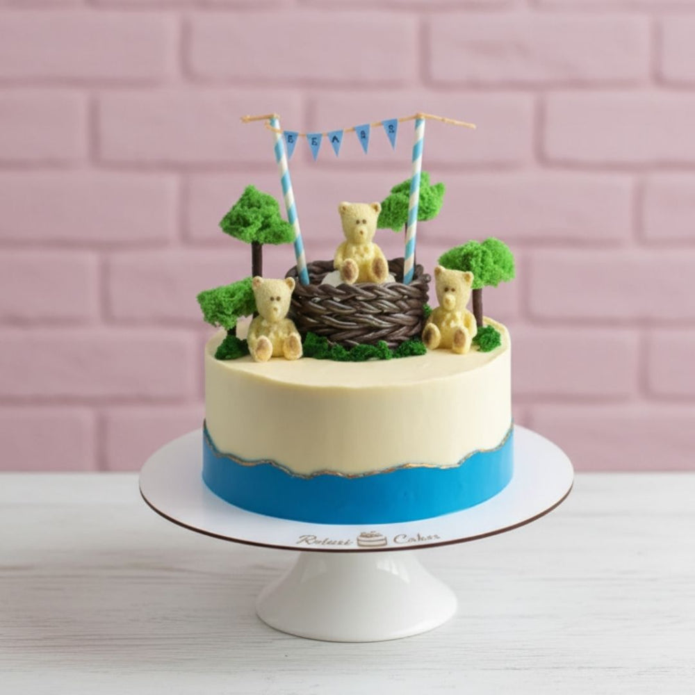 Decorative cake with teddy bears and a basket on a white stand against a pink brick wall.