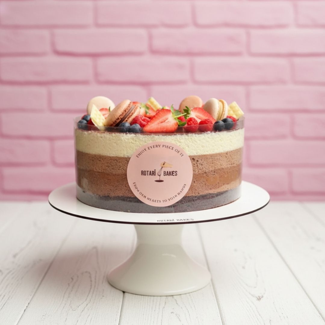 trio cake with berries & macarons on top on a white stand against a pink brick wall