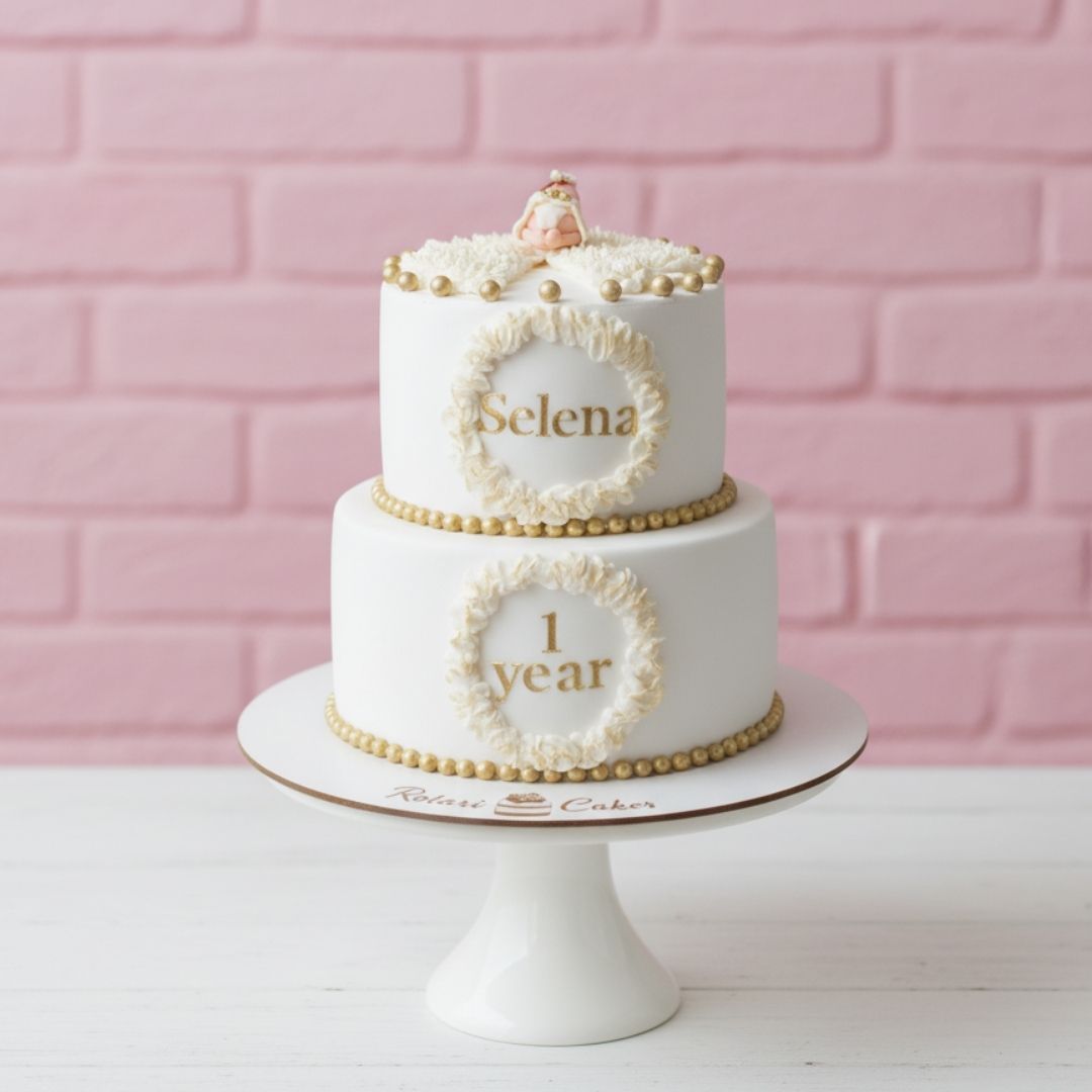 Two-tiered birthday cake with 'Selena' and '1 year' on a pink brick wall background