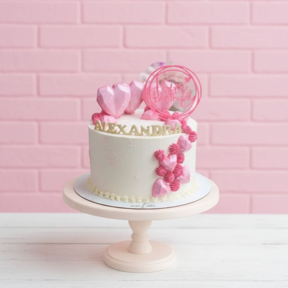 White cake with pink decorations on a pink brick wall background