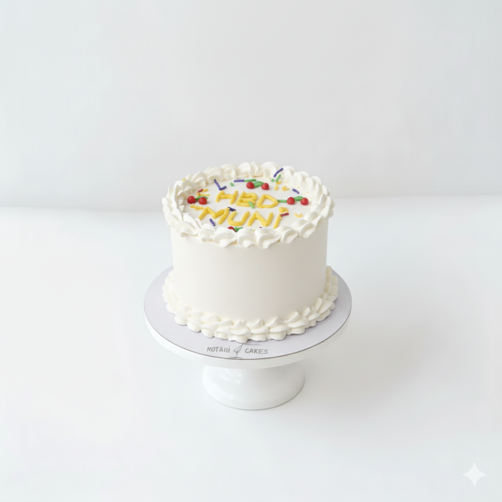 
                  
                    White cake with colorful lettering on a white stand against a white background
                  
                