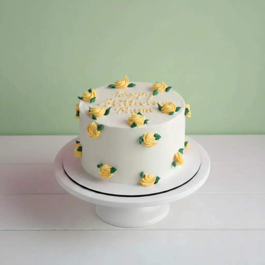 White cake with yellow roses on a white stand against a green wall